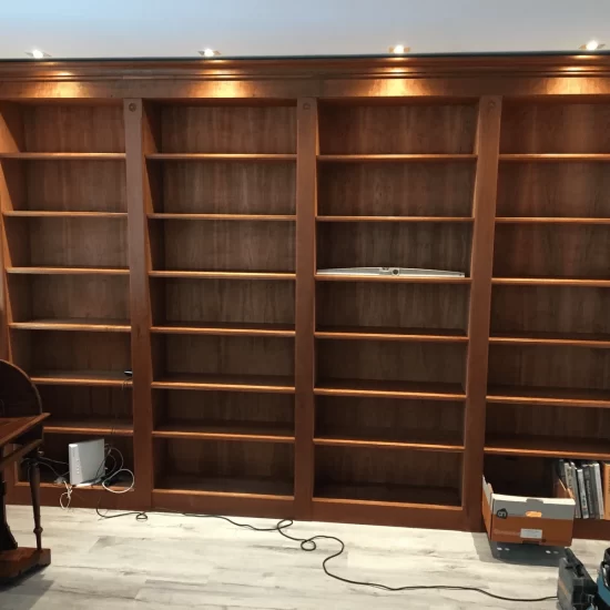 Een boekenkast met een klassiek uiterlijk van donker hout, bestaande uit vier delen, elk kastdeel heeft zeven planken en is verlicht door een spot in het plafond.