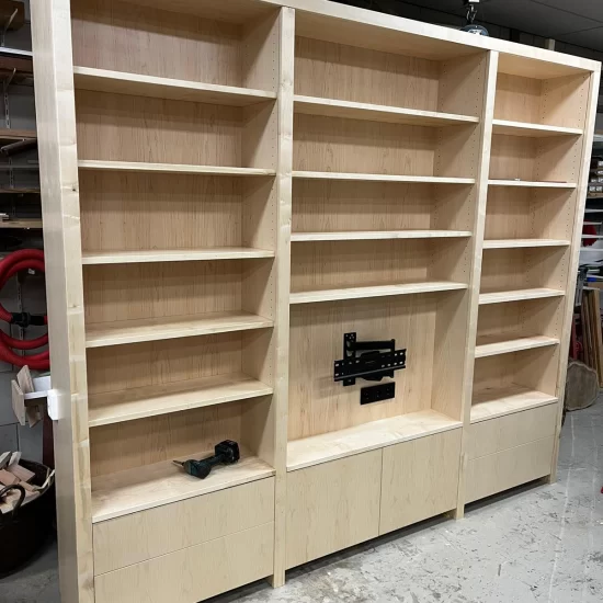 In de werkplaats van totaalhout wordt een lichtbruine houten boekenkast, bestaande uit drie delen, in elkaar gezet. De boekenkast heeft naast boekenplanken ook plek voor een televisie met onderin opbergruimten.