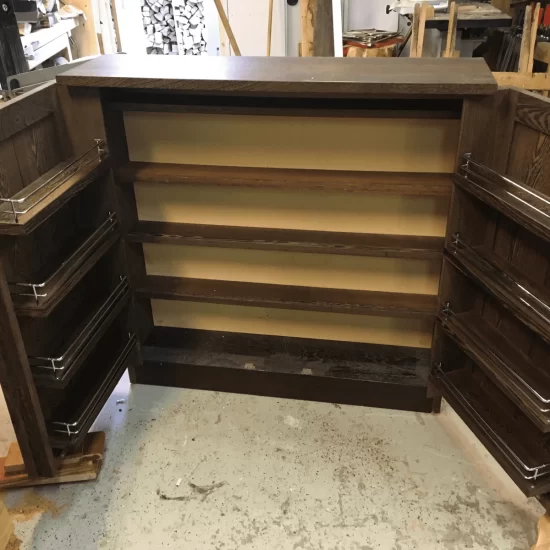 Een drankkast van massief donkerbruin hout met vier planken en twee opengeklapte deuren. Beide deuren hebben aan de binnenzijde vier planken en elk plank heeft een chroomkleurige rek om drank- en wijnflessen rechtopstaand in op te bergen.