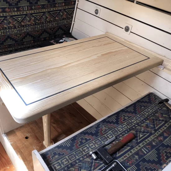 Een scheepstafel van lichtbruin hout met een inklapbaar voetstuk om de tafel naar de zijkant weg te bergen en vast te zetten.