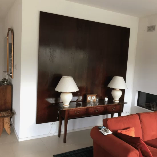 Een donkerbruin vierkante houten design wand met daarachter sfeerverlichting, gemonteerd op een witte muur in de woonkamer.
